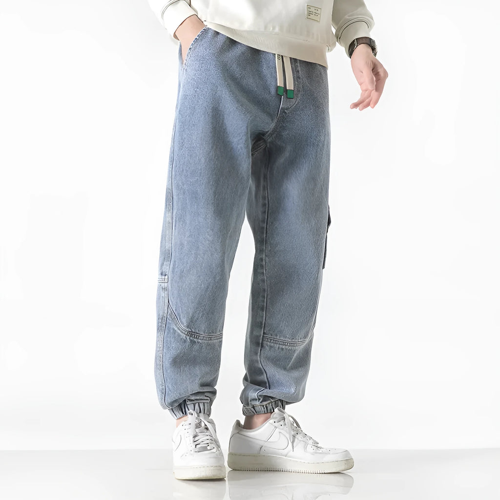 Men's loose-fit tapered cotton trousers in grey, shown on a model, featuring a mid-waist and tapered leg.