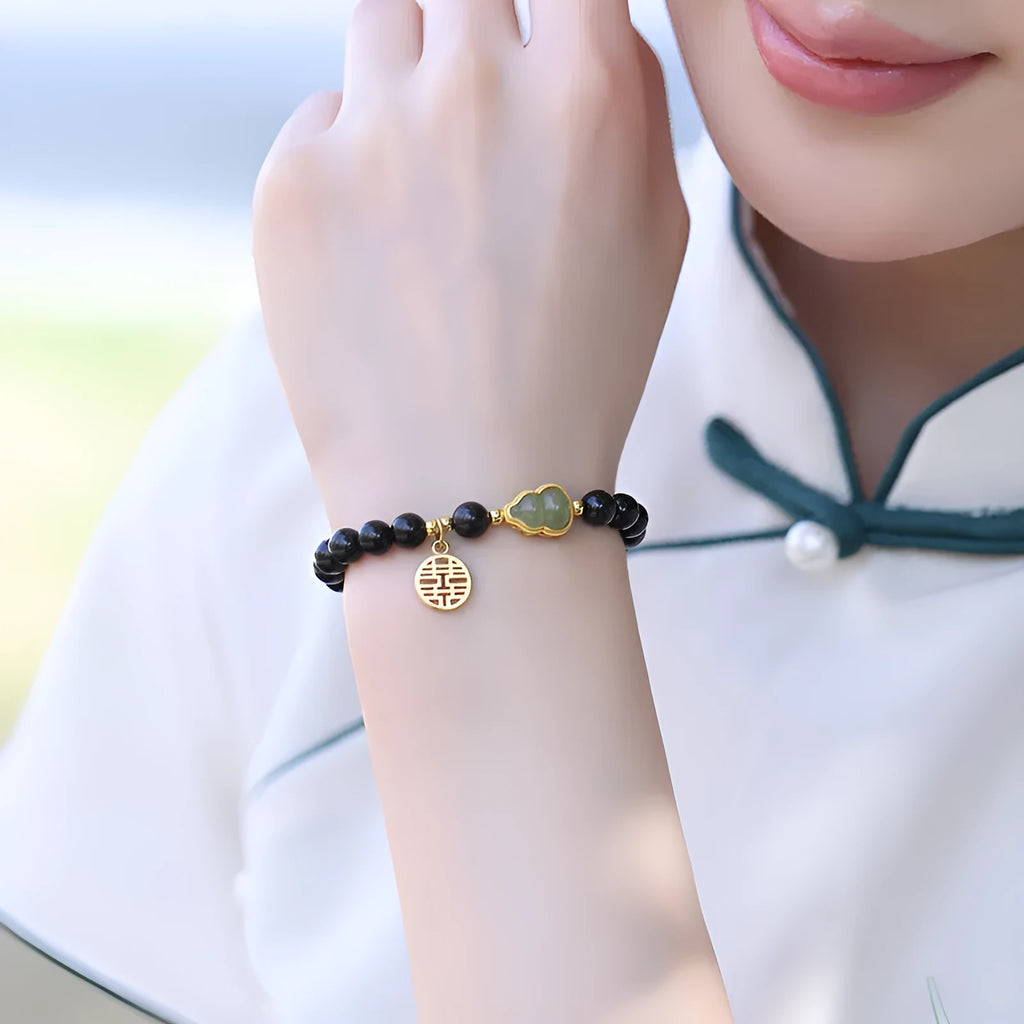 Black obsidian bead bracelet with a carved Hetian jade gourd charm in geometric pattern.