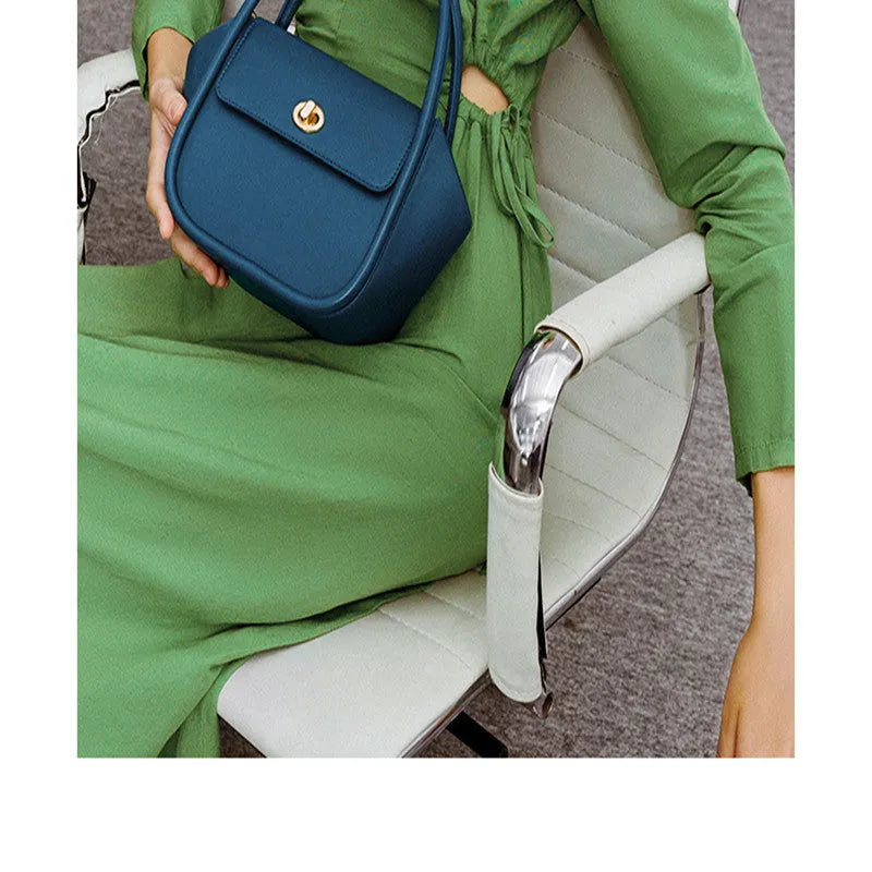 A women's leather wing-shaped tote bag with a metal latch, shown in blue on a cross-body strap.