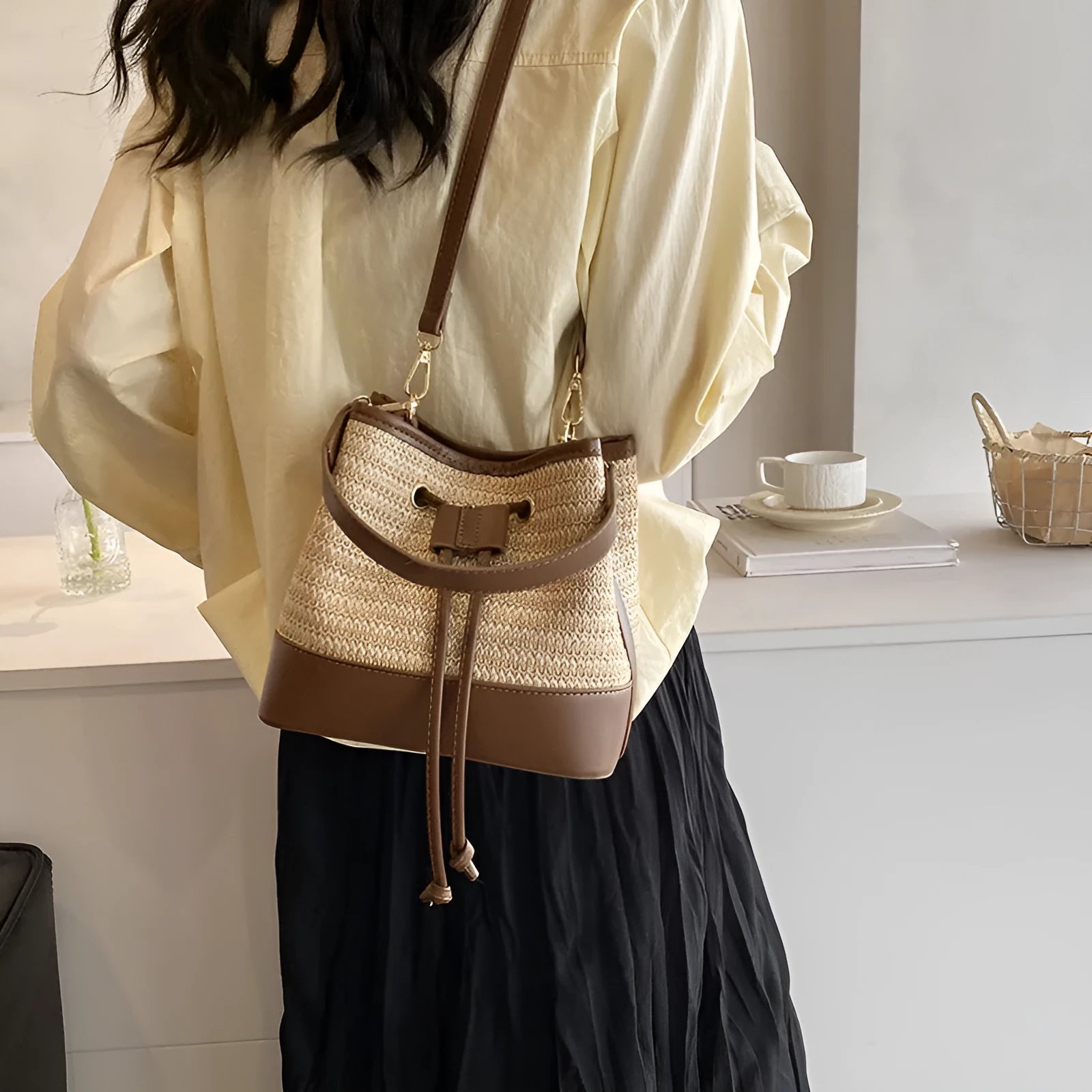 Brown woven straw women's crossbody bucket bag with adjustable strap on a table.