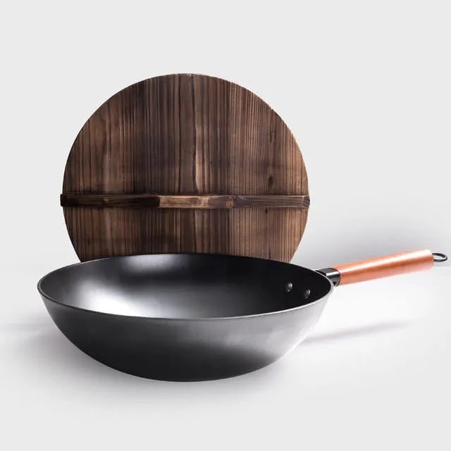 Handmade traditional black cast iron wok with wooden handle on a kitchen counter.