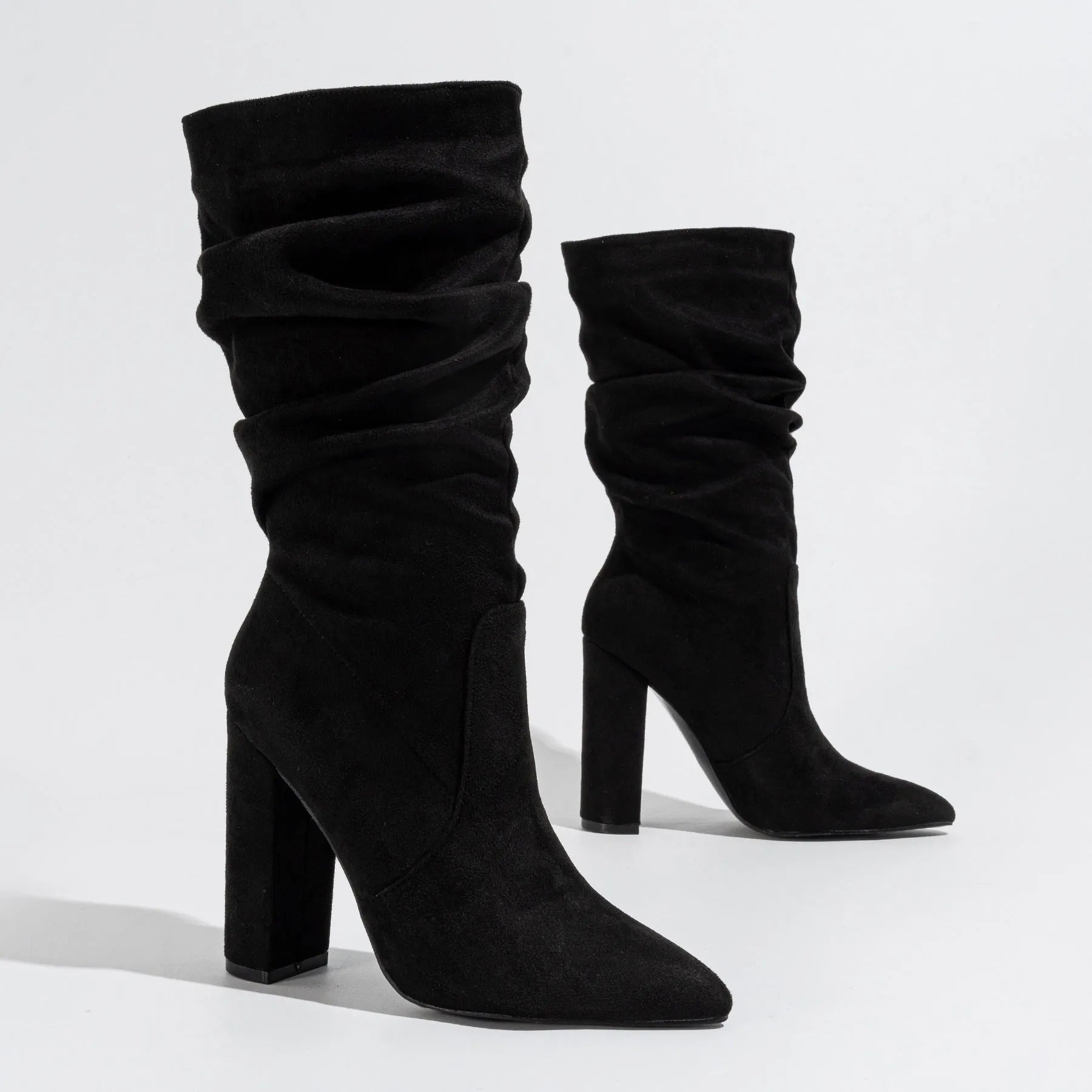 Women's black suede pointed-toe ankle boots with a chunky high heel, shown on a mid-calf.
