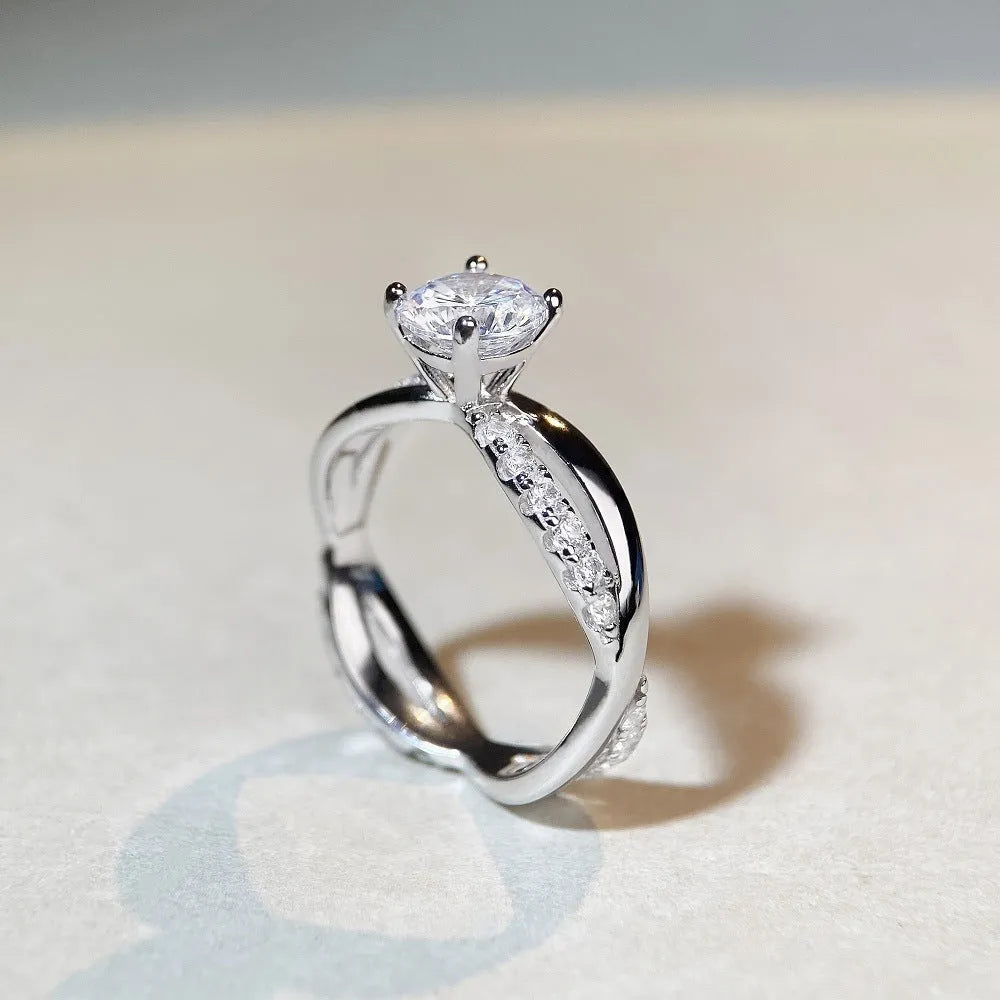 Silver ring with a 1 karat moissanite stone in a twisted four-claw setting, showing geometric lines and a cross design.