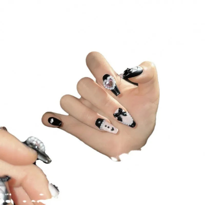 Black false nails with pink hand-painted peach hearts and bow design, shown in a cat's eye style.