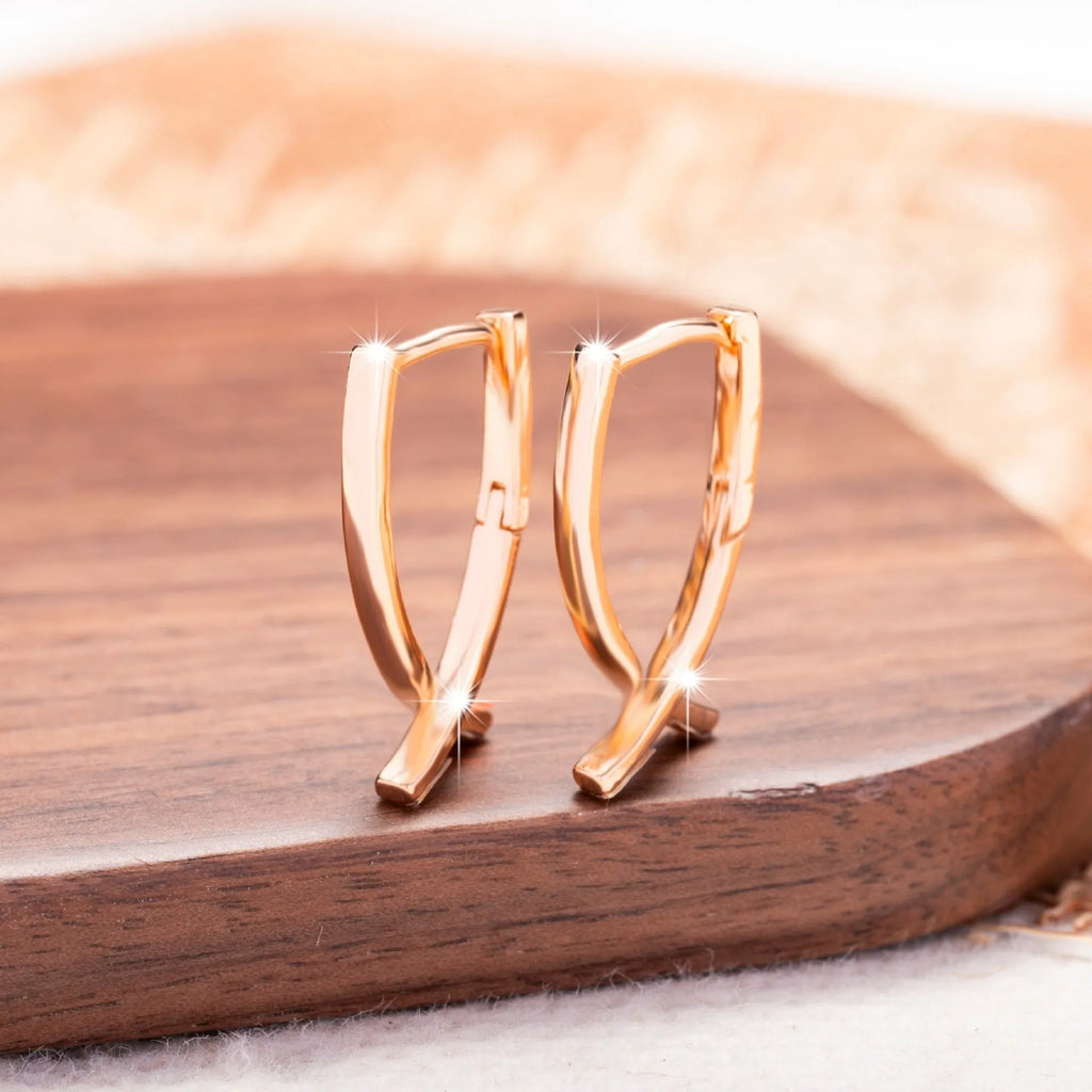 Rose gold cross shaped earrings on a plain background.