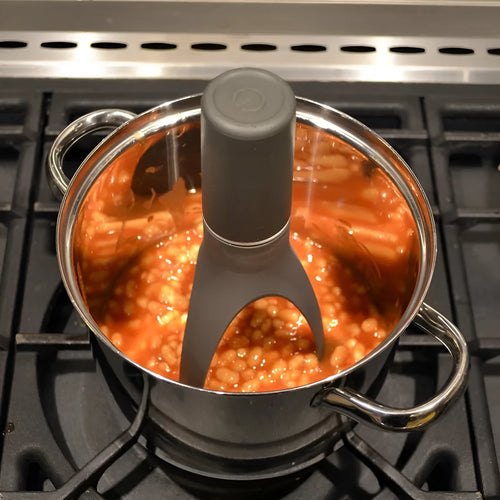 Green and grey automatic Stirr utensil for hands-free mixing in a cooking pot.