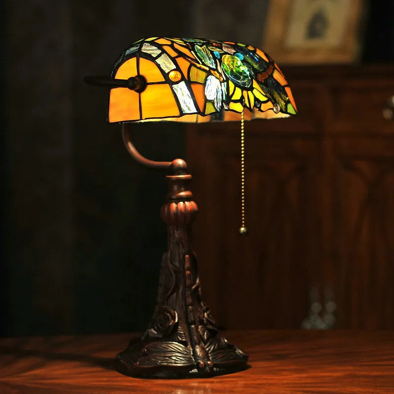 Tiffany style table lamp with coloured stained glass shade on a resin base, shown on a desk.