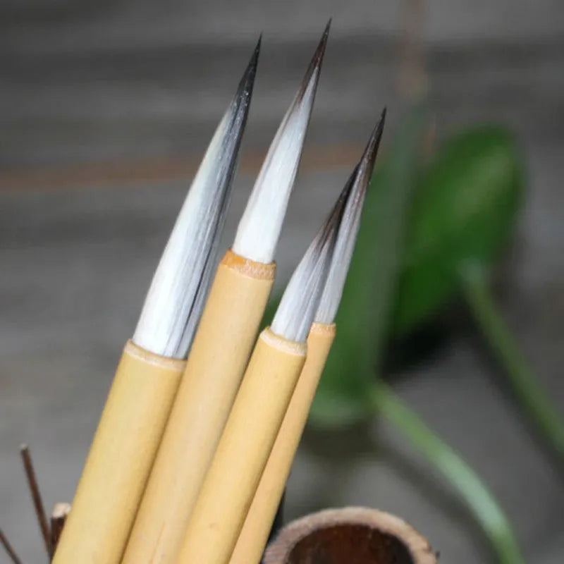 Four Chinese calligraphy brushes with thin gold bodies and natural hair bristles in pine branch colours