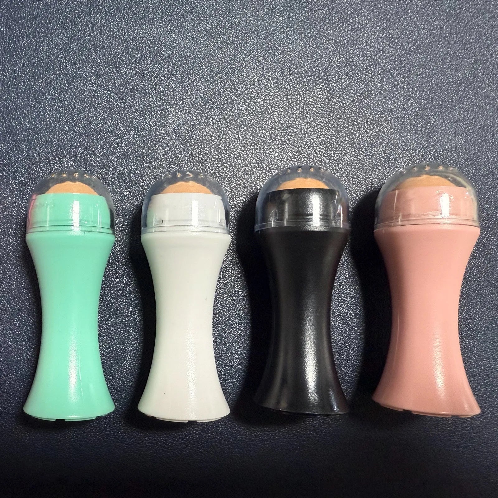 A small portable volcanic stone roller for absorbing facial oil, shown in various colours on a neutral background.