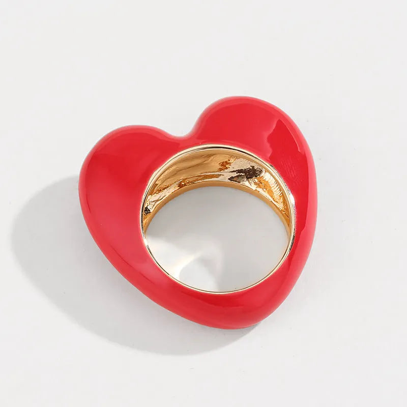 Heart-shaped zinc alloy ring with three-dimensional enamel colour in black, pink, purple, or red on a finger.