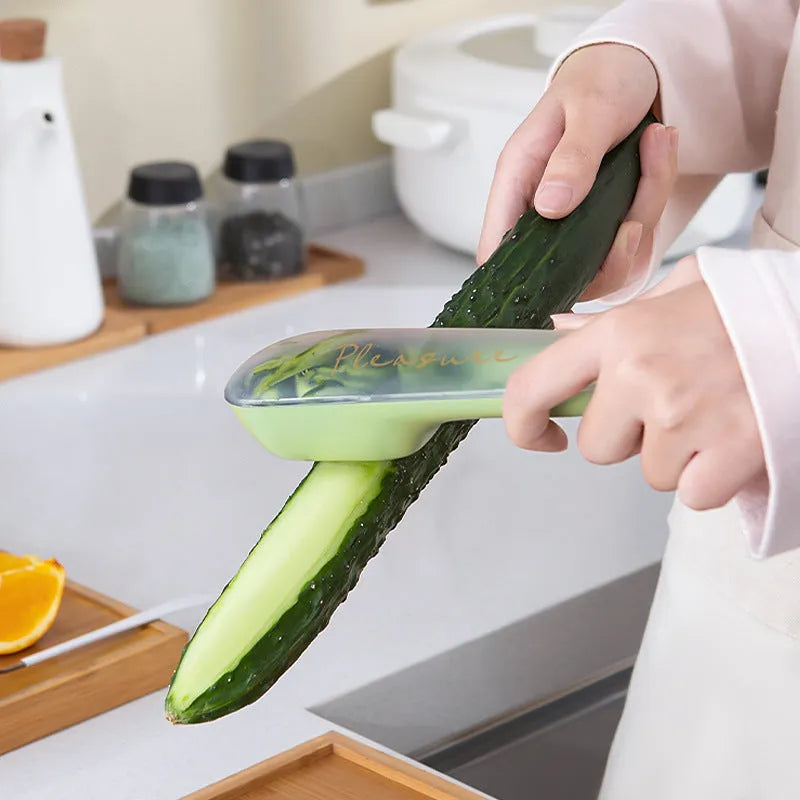 Dark green kitchen peeler with a storage tube extended, showing the stainless steel blade and a hanging hole on the handle.