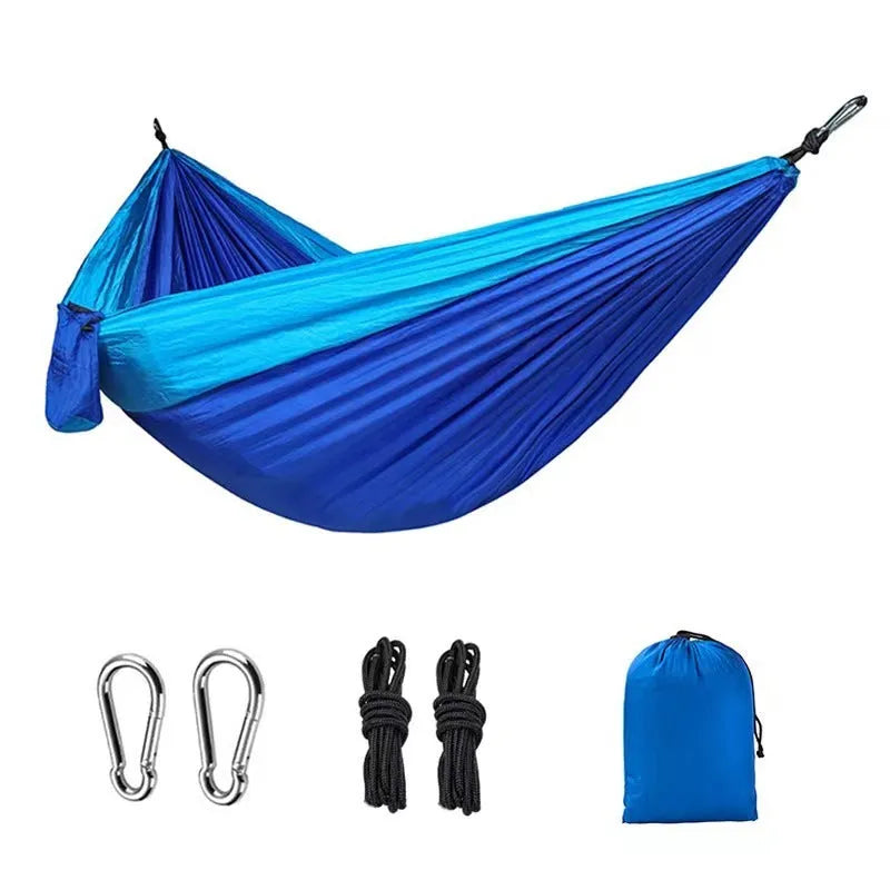 Sapphire blue parachute nylon hammock hung between two trees, showing its full 270cm length and integrated ropes.