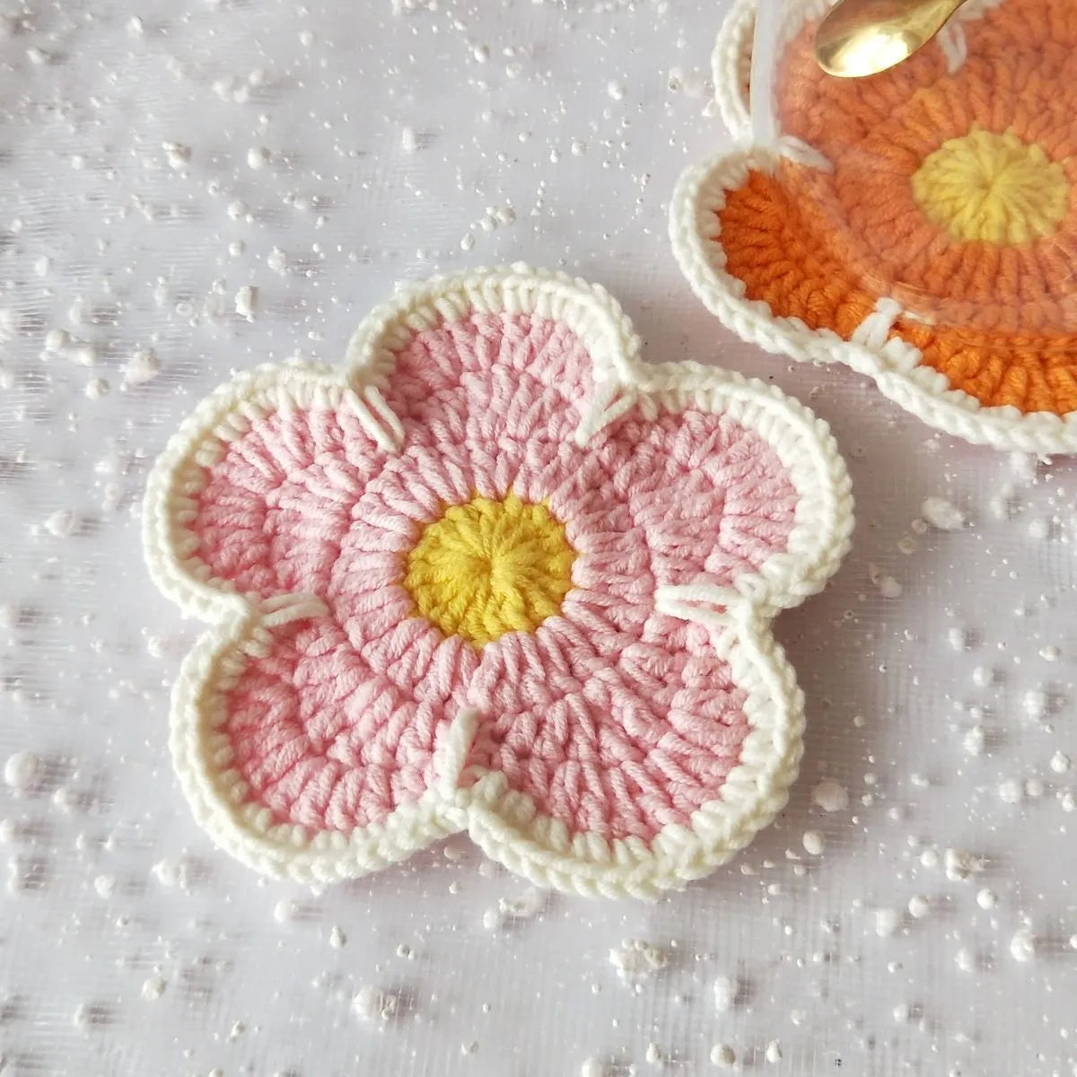 Set of five handmade woven flower placemats in blue, green, orange, pink, and purple colours on a wooden table.