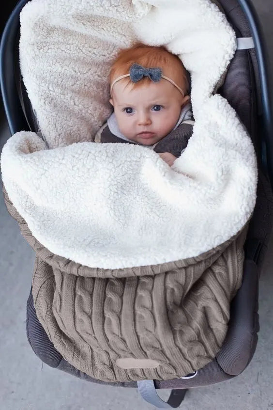 Envelope-style baby stroller sleeping bag in beige colour with thick filling, shown next to a pram.