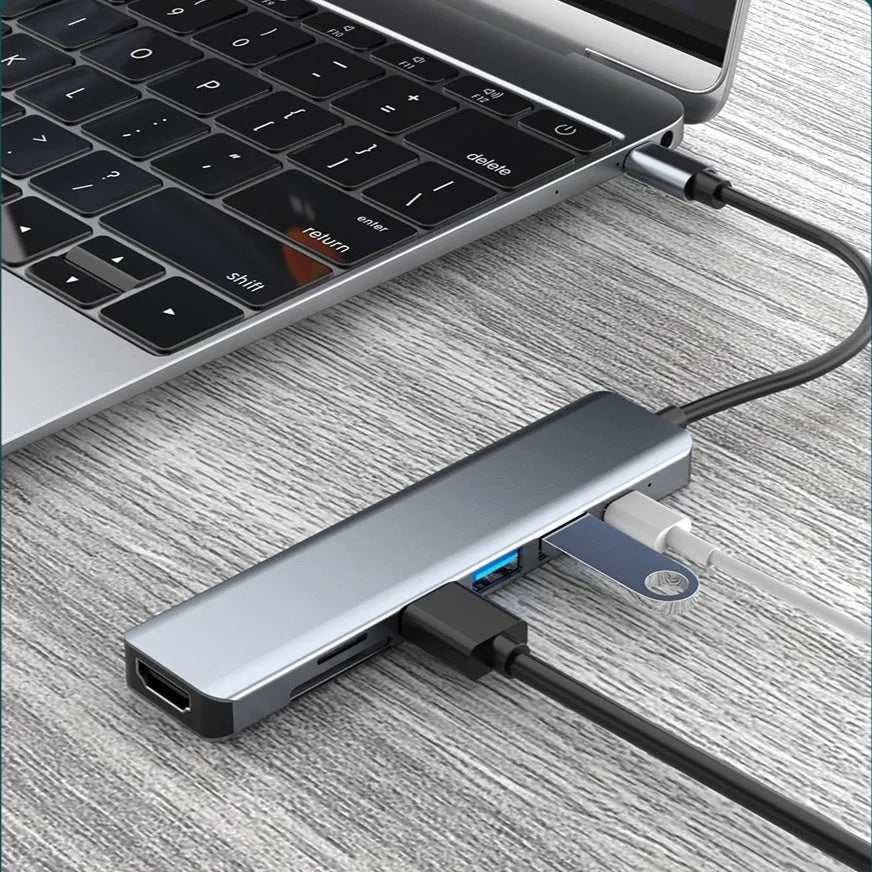 Silver seven-port type-C USB expander hub with a short black cable on a wooden desk.