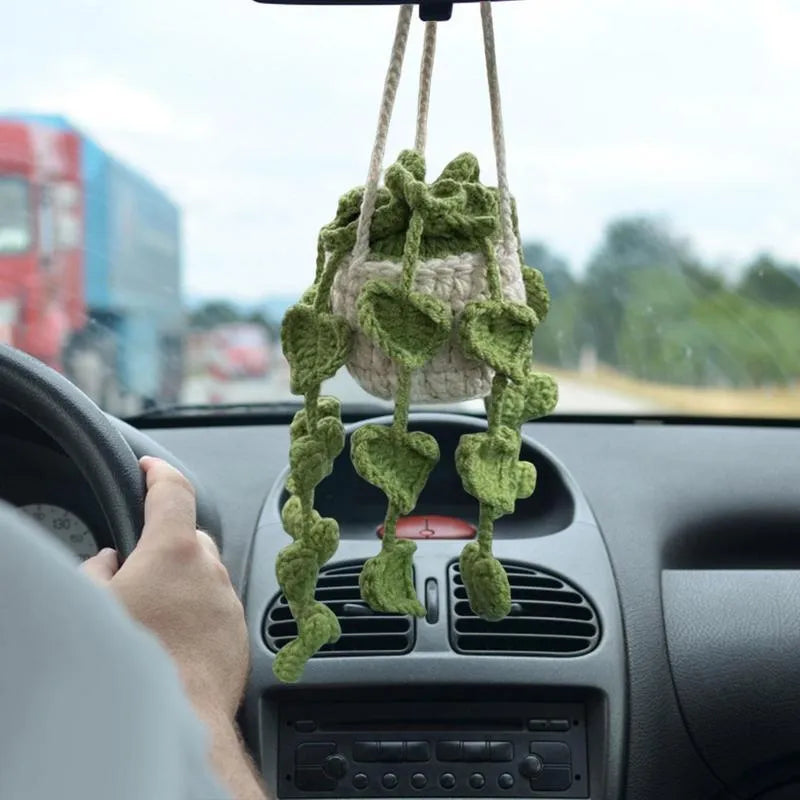 Green and white knitted wool car plant decoration with small basin and hanging rope.