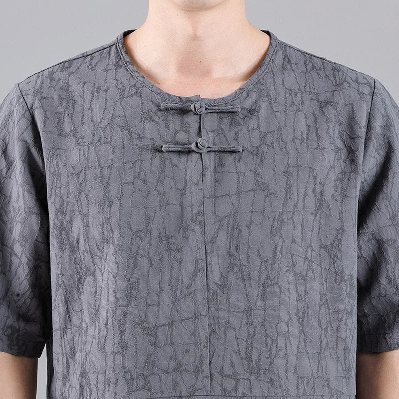 Man wearing a black loose-fit linen t-shirt with a retro jacquard pattern and fastener decoration.