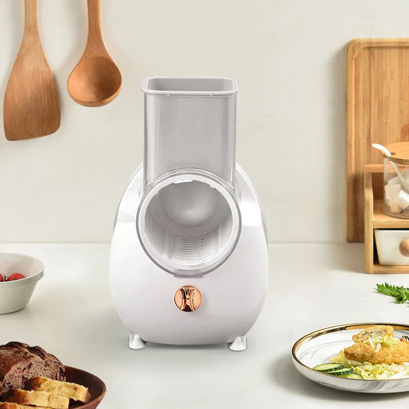 White electric vegetable slicer with rotary grater, suction base, and set of three blade pairs on a kitchen worktop.