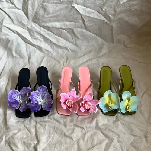 Pink women's sandals with artificial Phalaenopsis flower, satin upper, and mid heel.
