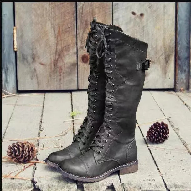 Black chunky heel high leg boots with a round toe and low heel on a plain background.