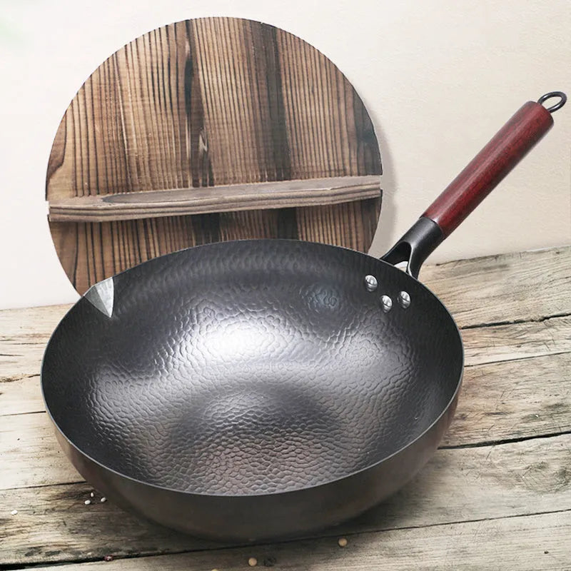 Handmade traditional black cast iron wok with wooden handle on a kitchen counter.