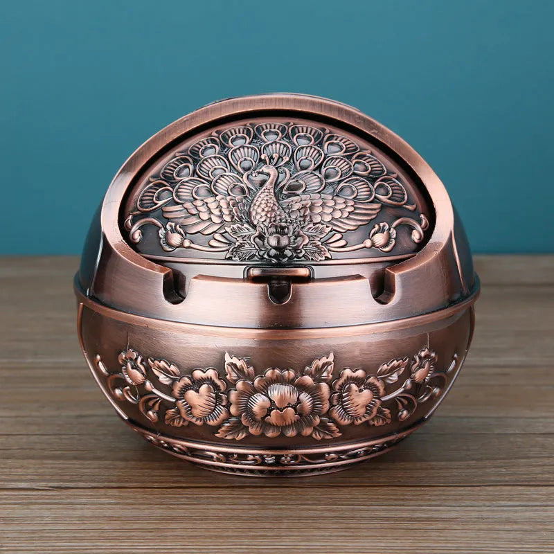 Alloy decorative ashtray in bronze with ornate peacock motif and cigarette extinguishing slot.