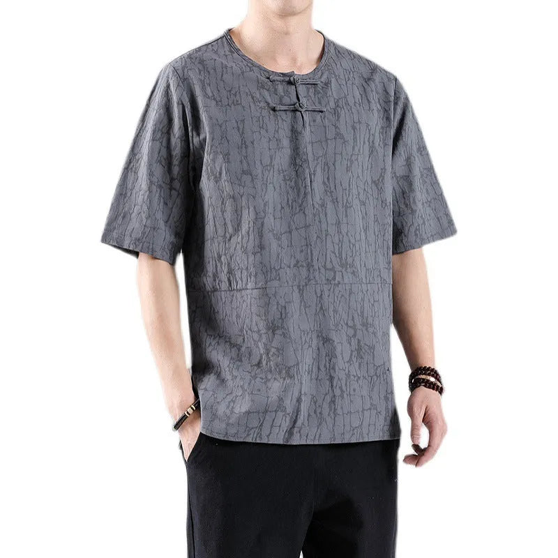Man wearing a black loose-fit linen t-shirt with a retro jacquard pattern and fastener decoration.