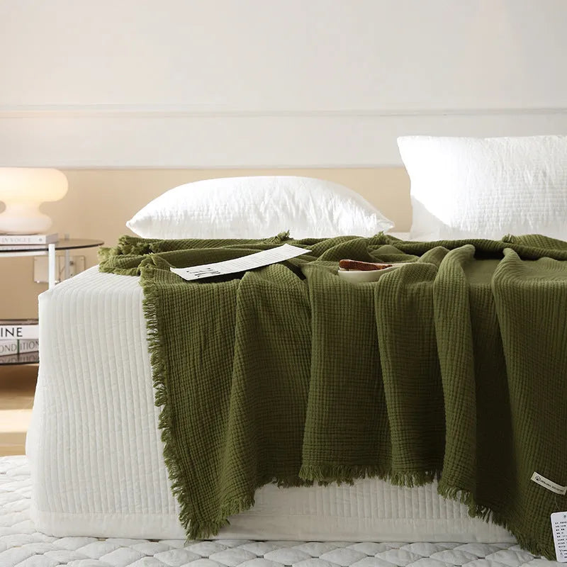 Four-layer gauze cotton blanket with tassel edging in avocado green, laid flat.