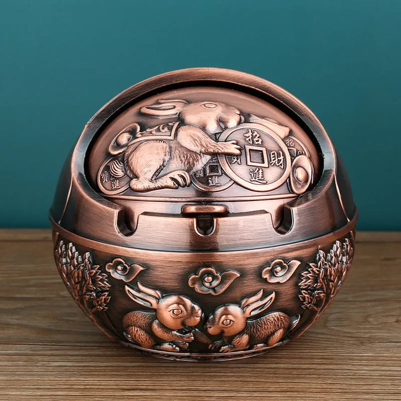 Alloy decorative ashtray in bronze with ornate peacock motif and cigarette extinguishing slot.