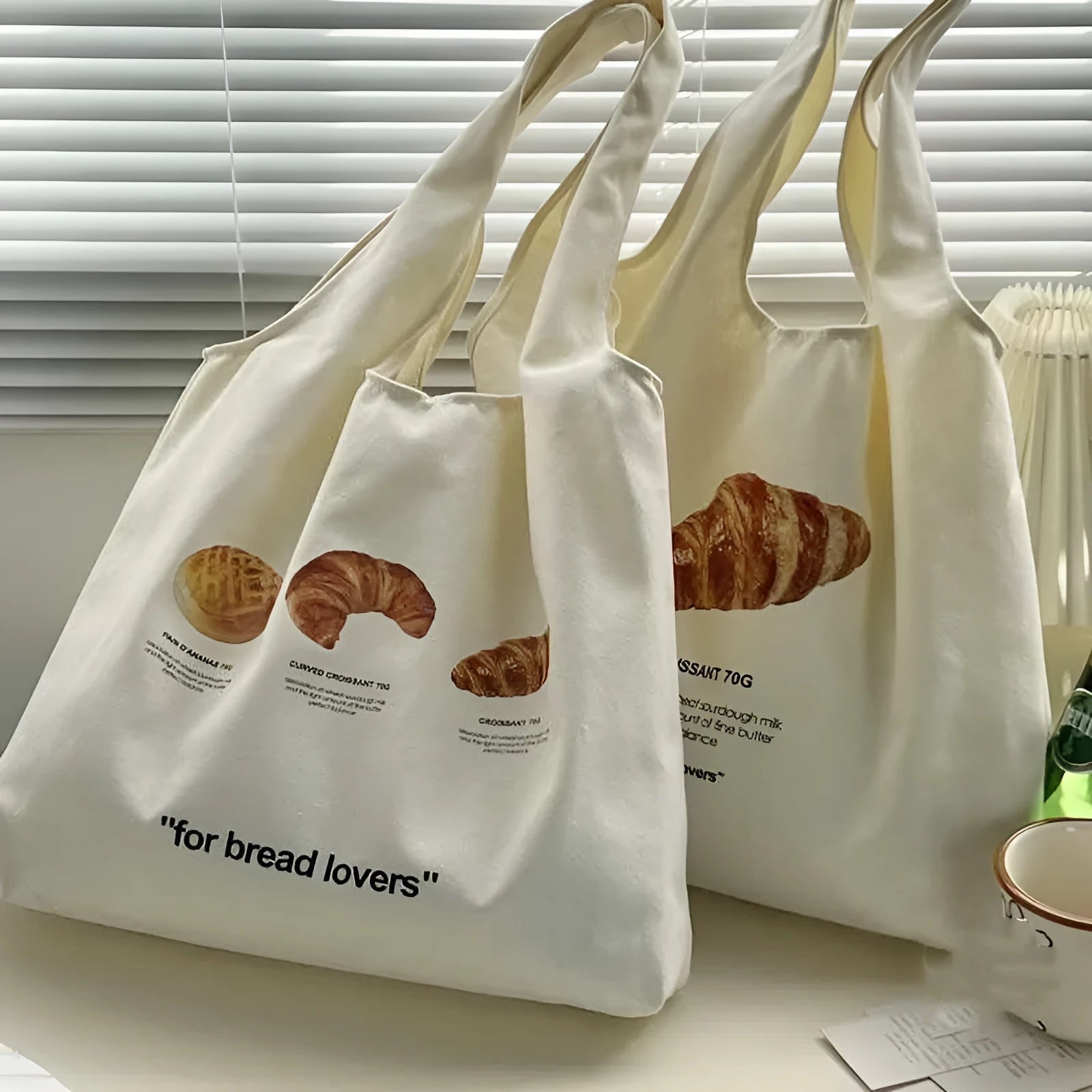 Beige canvas shoulder bag with croissant and bread print showing front panel design and shoulder strap