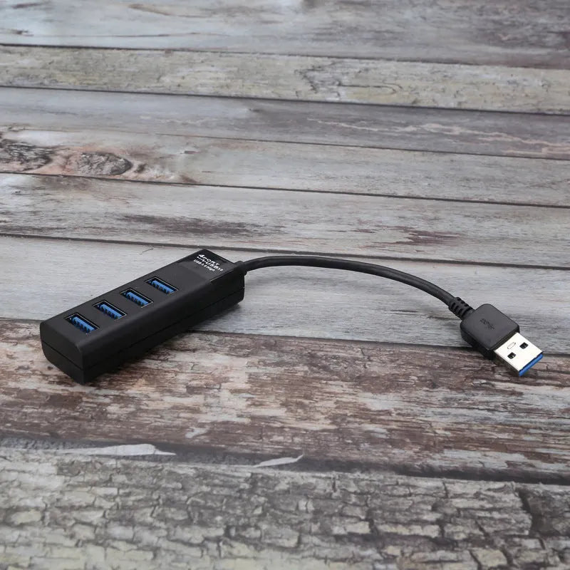 Black USB 3.0 hub with four ports, LED indicators, and a 30 cm attached cable on a desk.
