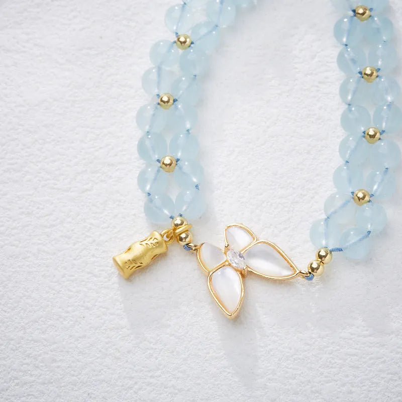 Close-up of a women's woven bracelet with a butterfly motif and a central aquamarine gemstone bead.