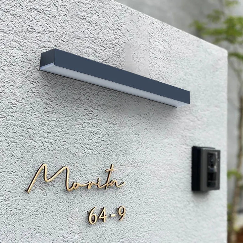 Black solar-powered outdoor wall lamp with integrated solar panel, mounted on a garden wall.