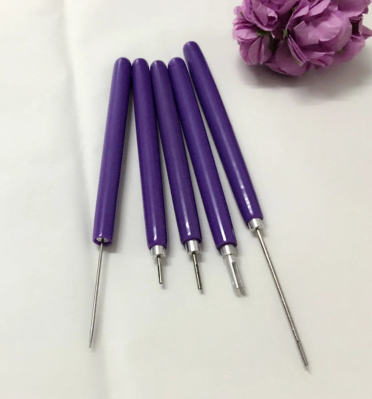 Five purple quilling pens with slotted tips and a stylus laid out on a surface
