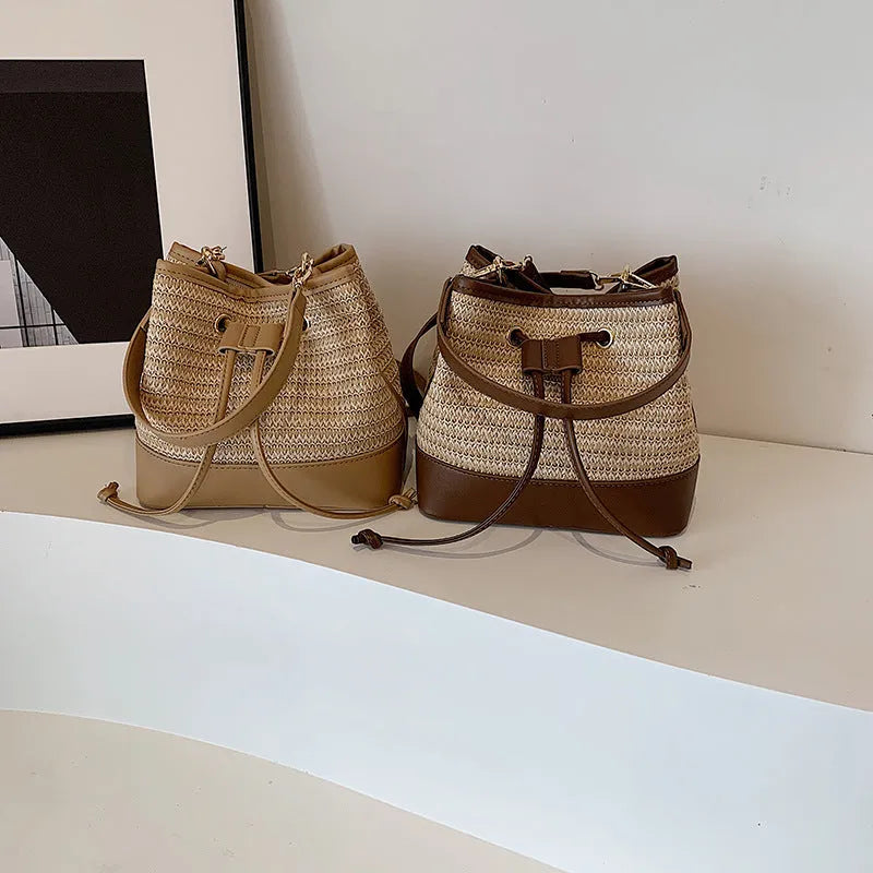 Brown woven straw women's crossbody bucket bag with adjustable strap on a table.