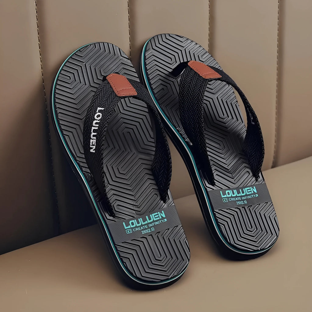 Men's black flip flops with a textured non-slip sole on a sandy beach background.