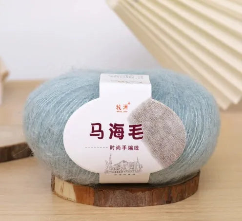 A ball of mohair yarn in a selected colour next to a hand-woven scarf example, showcasing the DIY kit.