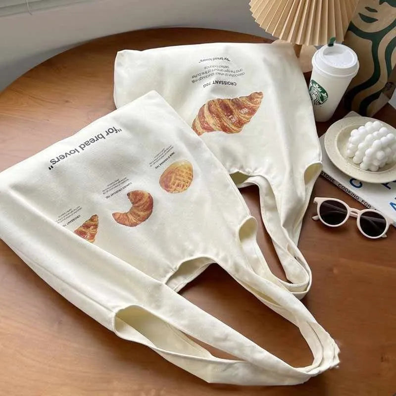 Beige canvas shoulder bag with croissant and bread print showing front panel design and shoulder strap