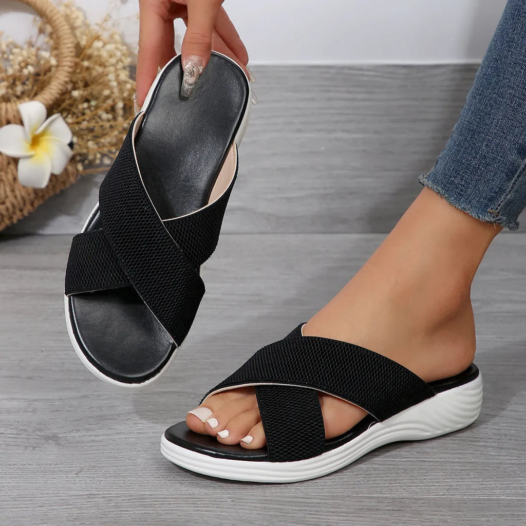 Black women's peep-toe slippers with a cross strap and thick flat rubber wedge sole.