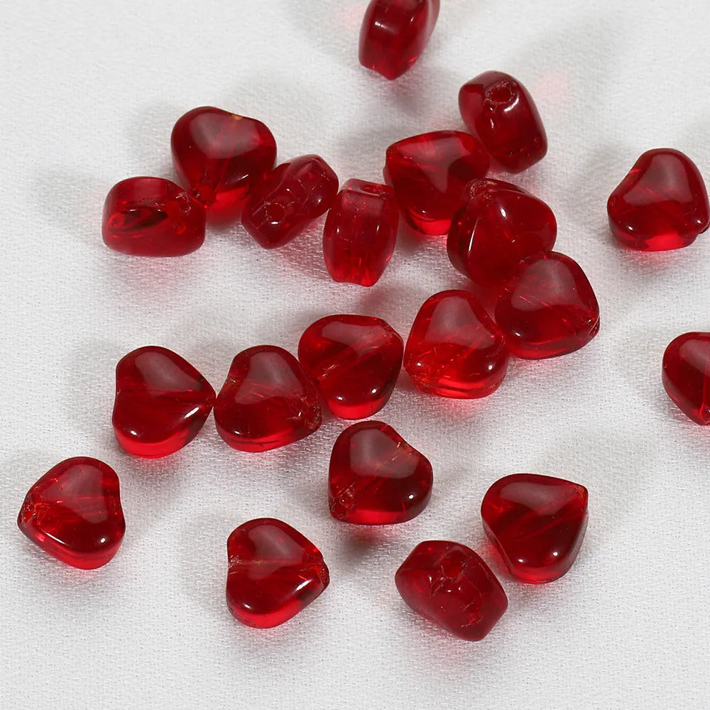 Twenty transparent love heart shaped spacer beads in assorted colours on a white background.