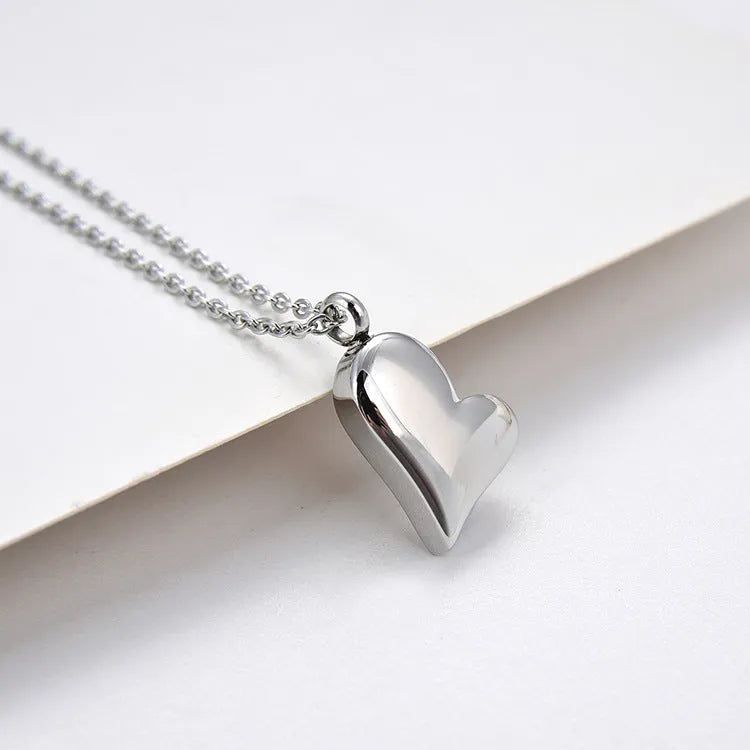 Silver curved peach heart pendant necklace with adjustable chain on grey background