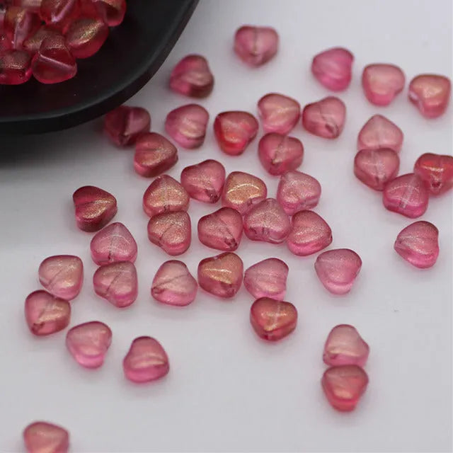 Twenty transparent love heart shaped spacer beads in assorted colours on a white background.