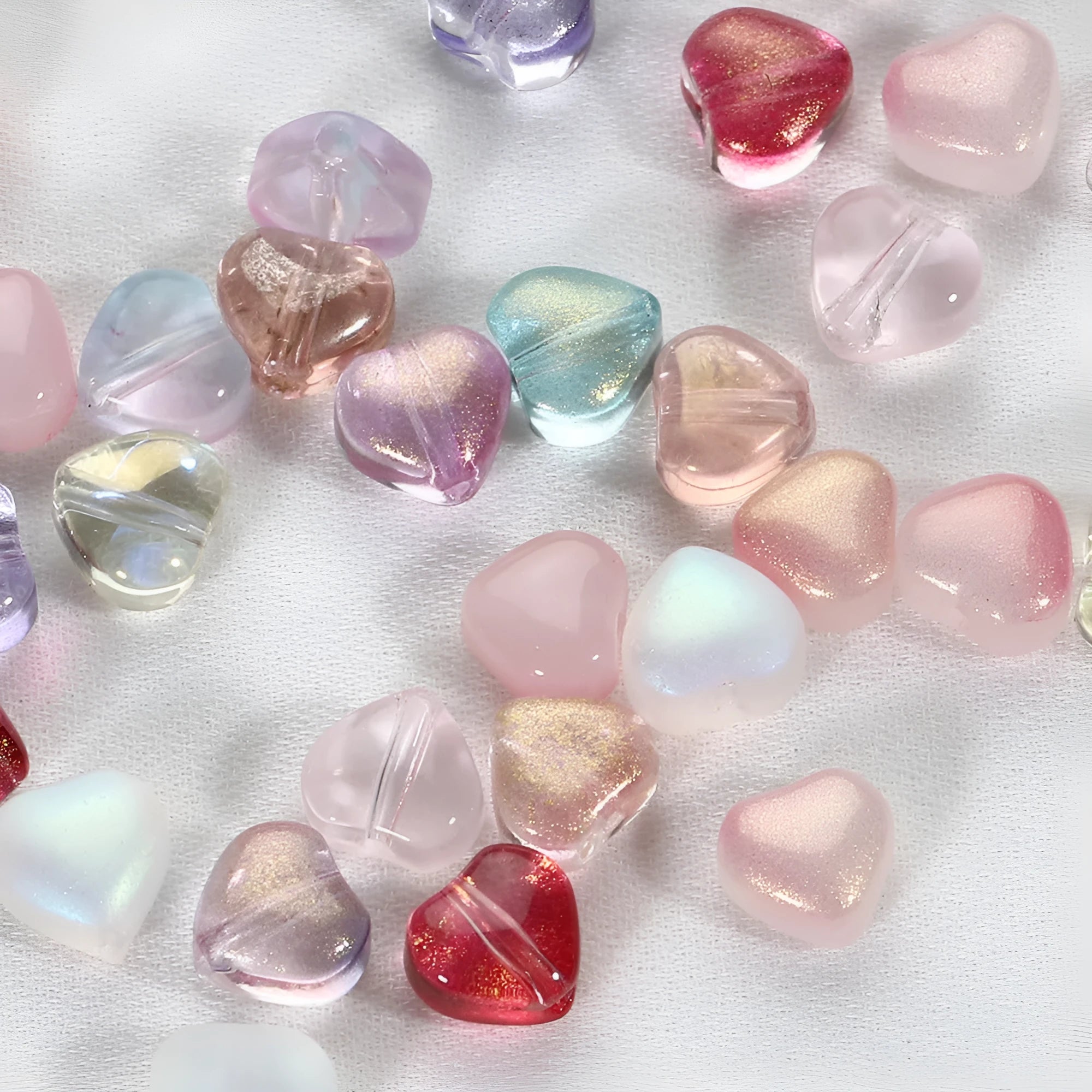 Twenty transparent love heart shaped spacer beads in assorted colours on a white background.