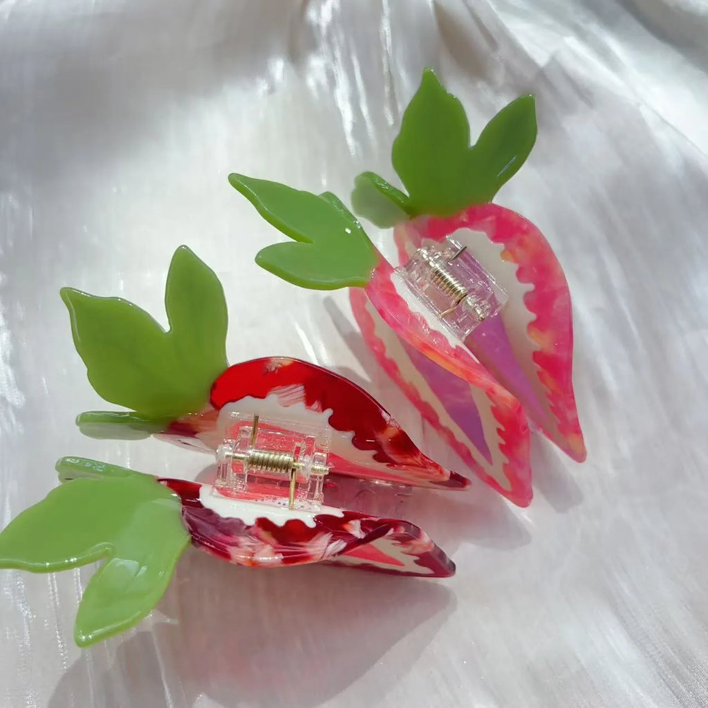 Close-up of a handmade strawberry decorative hair clip on a pink background.