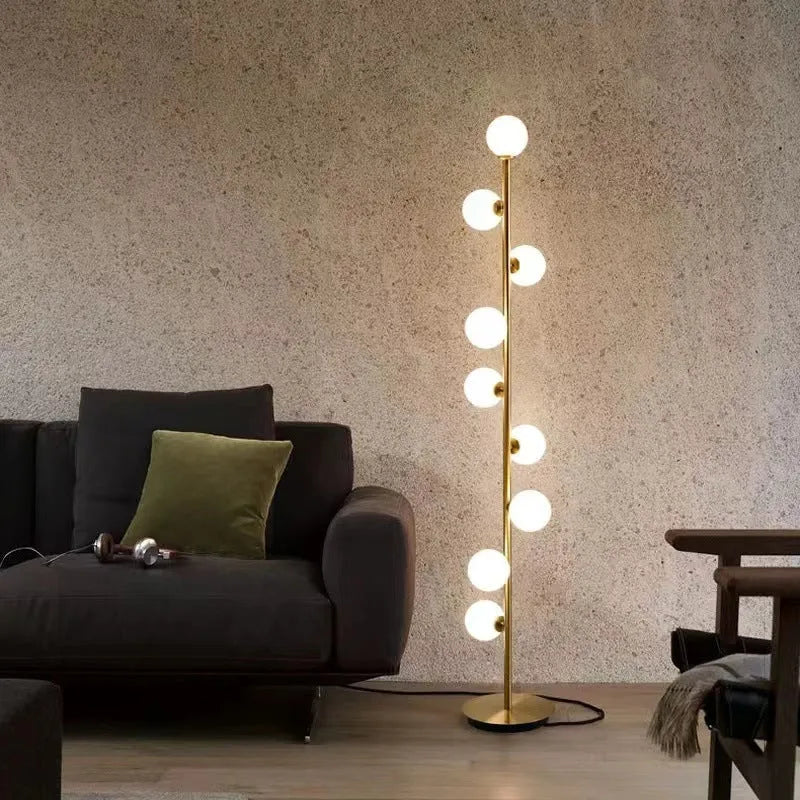 Tall modern floor lamp with slender iron frame, glass shade, and solid circular base in a minimalist living room setting.