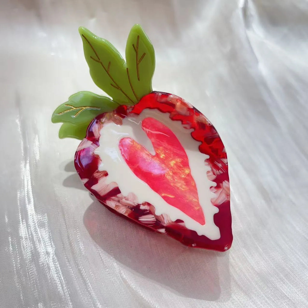 Close-up of a handmade strawberry decorative hair clip on a pink background.