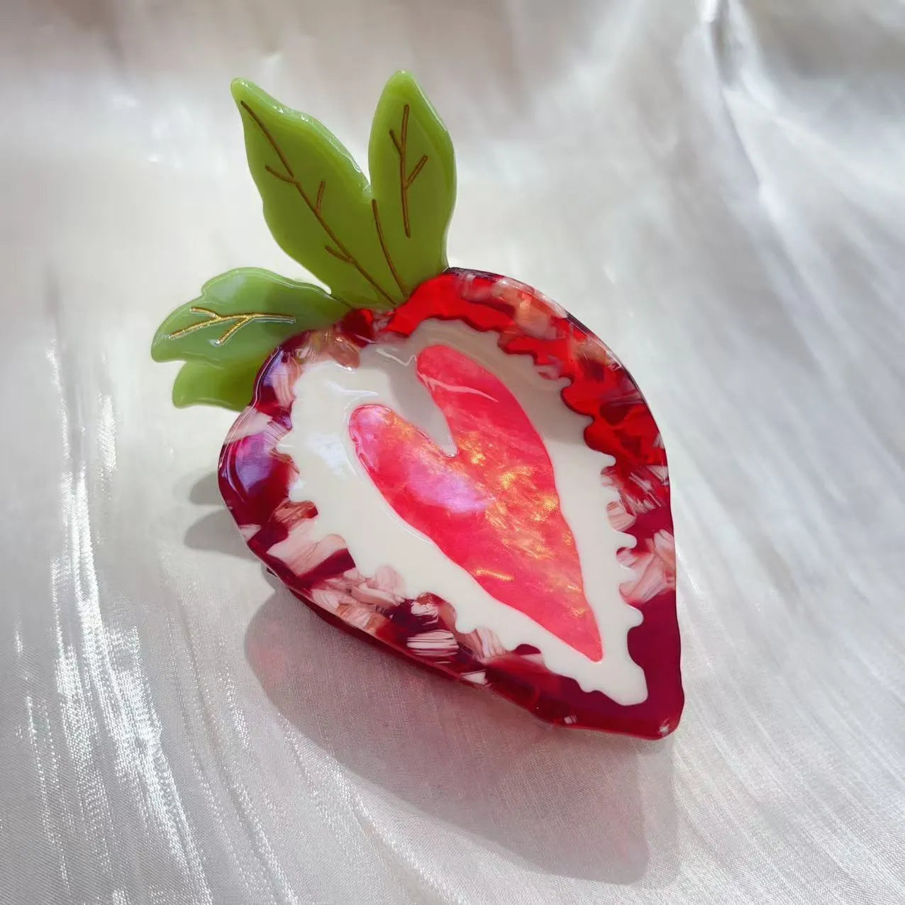Close-up of a handmade strawberry decorative hair clip on a pink background.