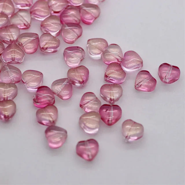 Twenty transparent love heart shaped spacer beads in assorted colours on a white background.
