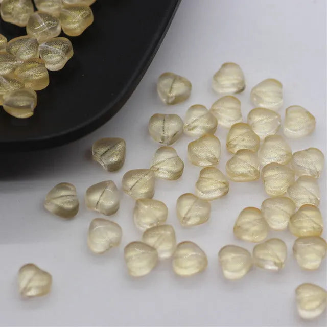 Twenty transparent love heart shaped spacer beads in assorted colours on a white background.