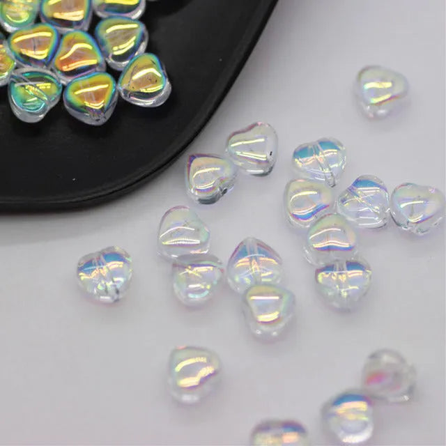 Twenty transparent love heart shaped spacer beads in assorted colours on a white background.